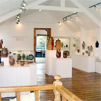 View across The Gallery Upstairs showing pots for sale by David and John Leach and glass cabinets with loaned pots by David and Bernard Leach