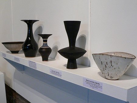 Tall black Hans Coper vase surrounded by Lucie Rie pots